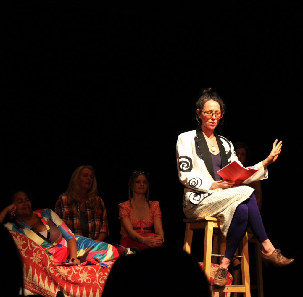 Woman sitting on stool on stage reading