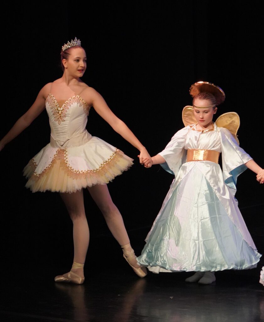 A professional ballerina guides a young dancer dressed as an angel.