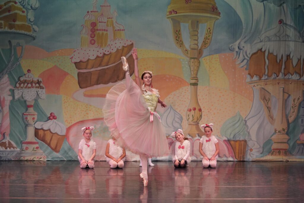 A professional ballerina dances in front of young dancers as lambs in the Nutcracker.