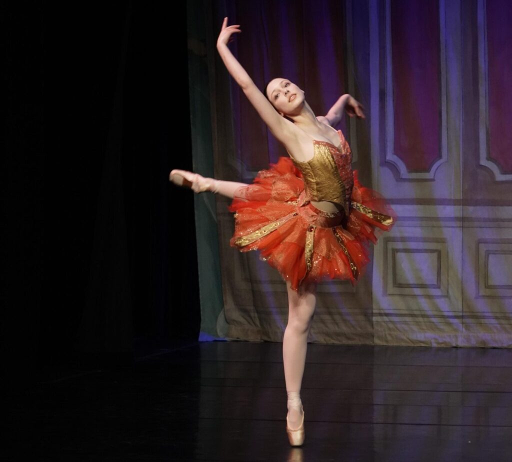 Ballerina on pointe in red tutu against dark background in the Nutcracker.