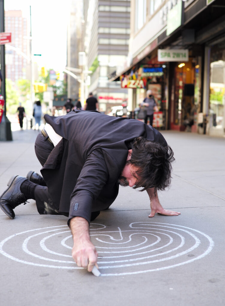 man drawing spiral labyrinth on city sidewalk
