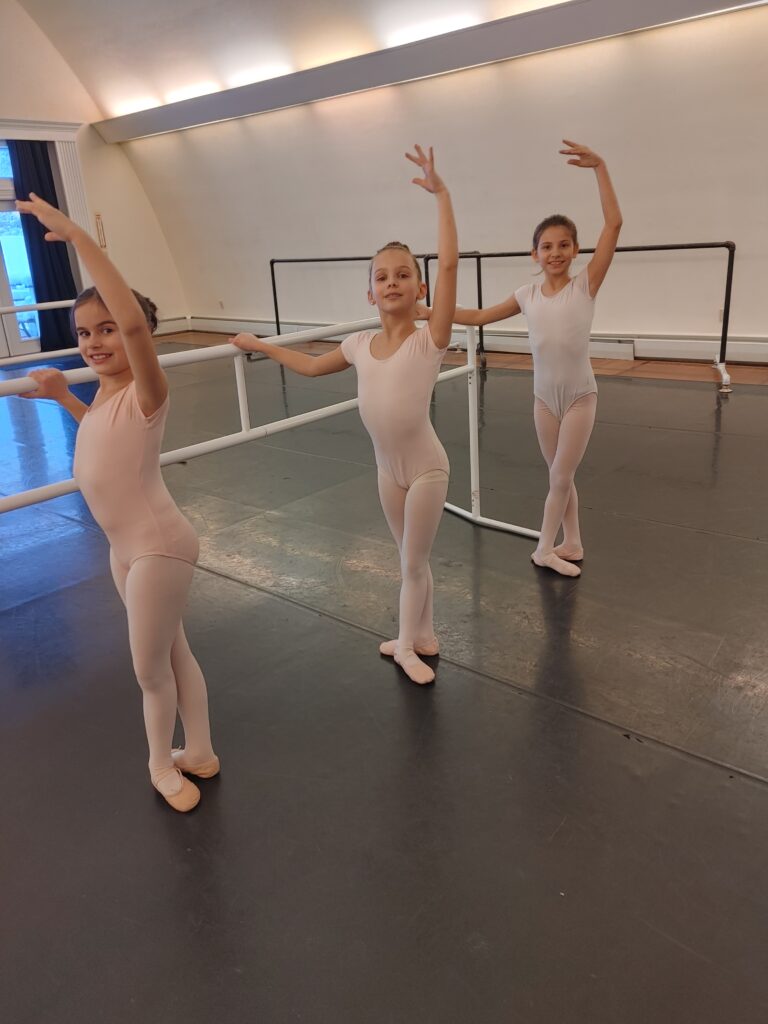 Three young girls in pink at ballet barre.