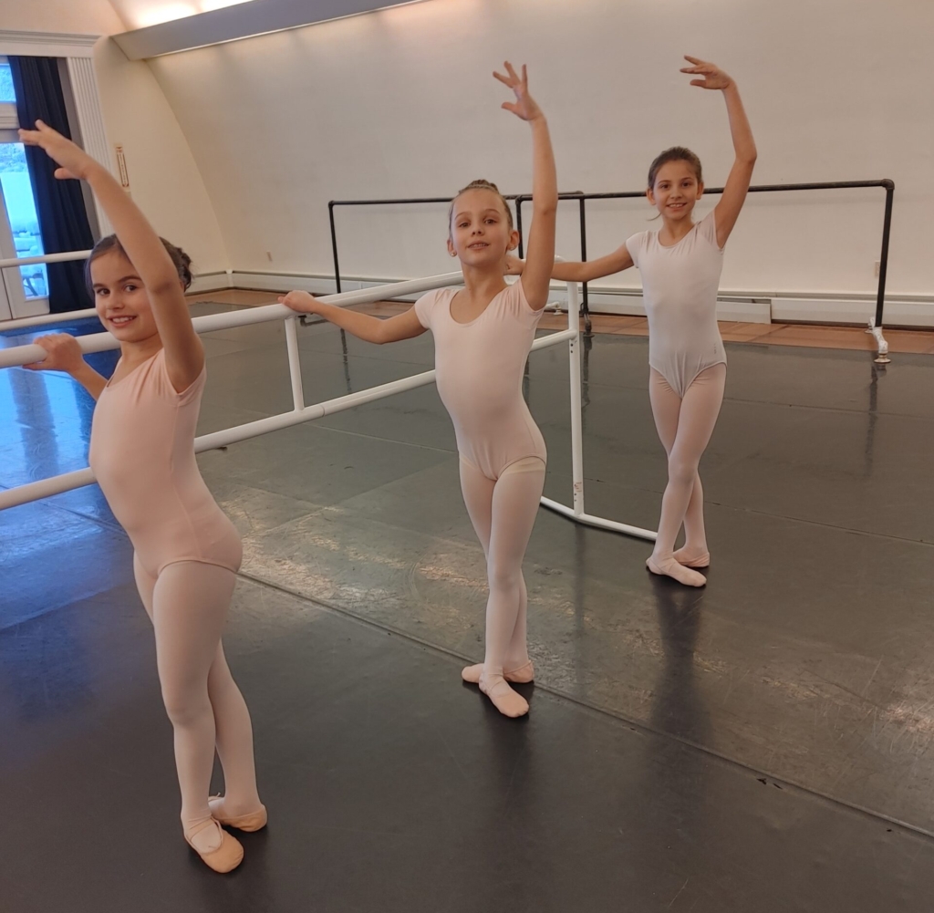 Three young girls in pink at ballet barre.