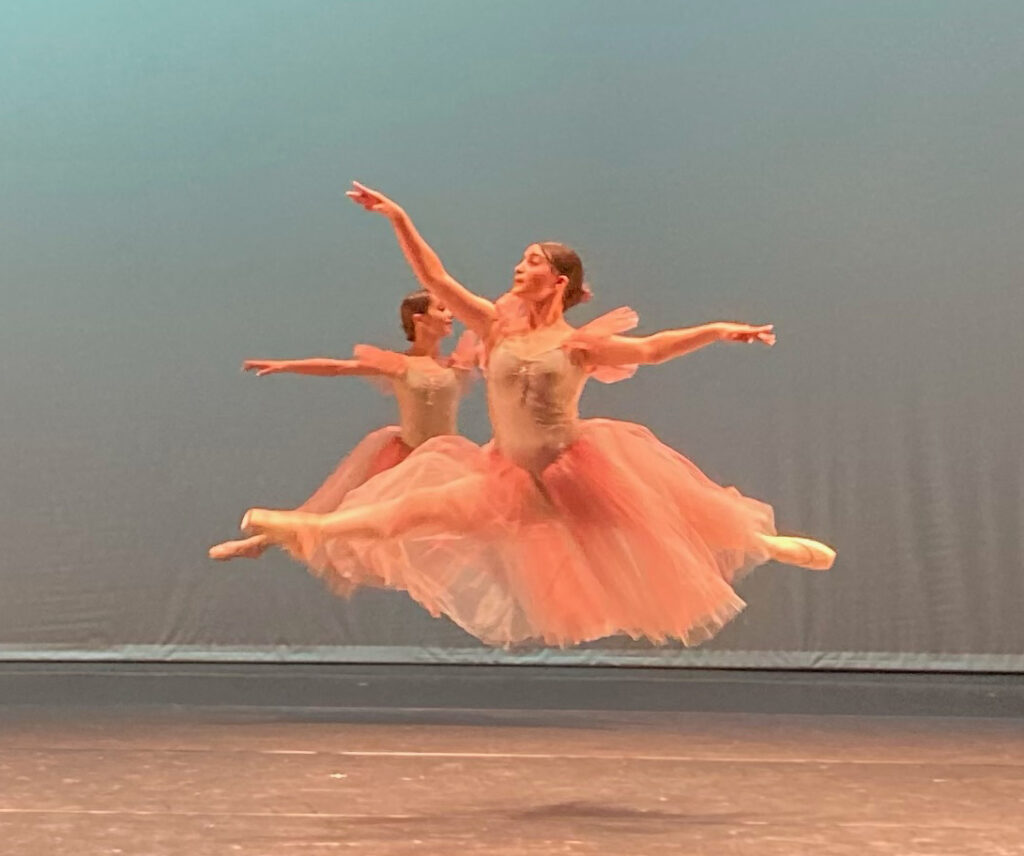 Two ballerinas in pink leaping across stage