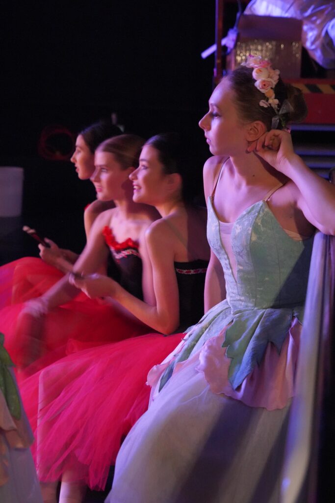 Four ballerinas in costume sit backstage