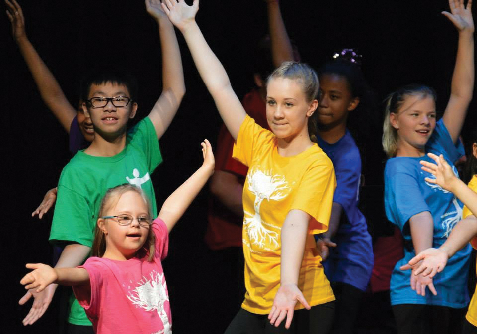 Kids in colorful tee shirts dance with arms outstretched