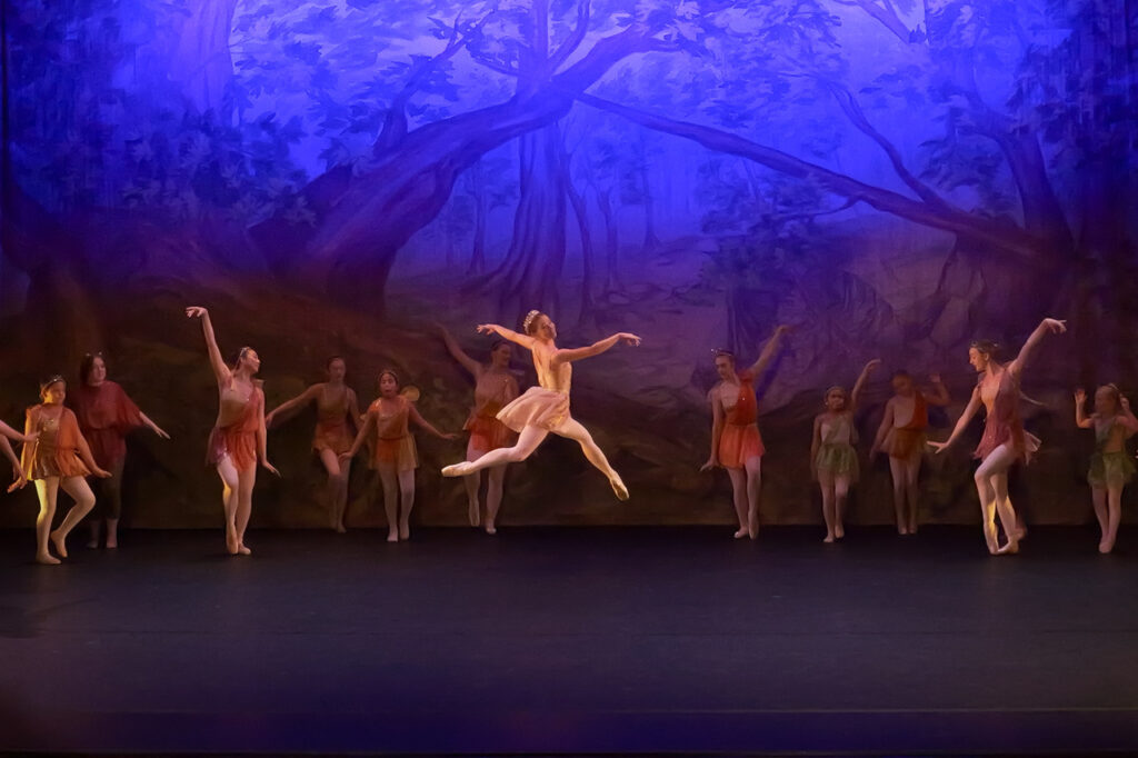 Solo dancer leaps in front of a background with a line of dancers