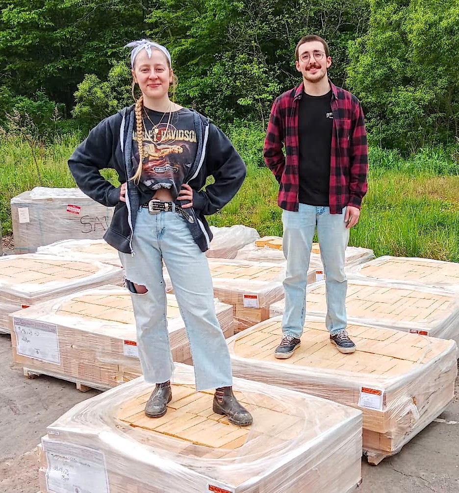 Two young people stand on pallets stacked outside.