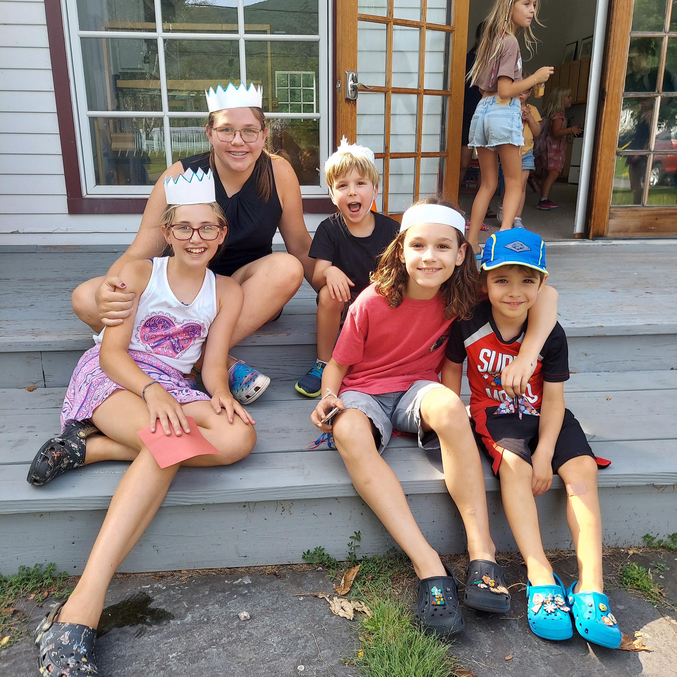A group of five kids in homemade crowns sit on steps together