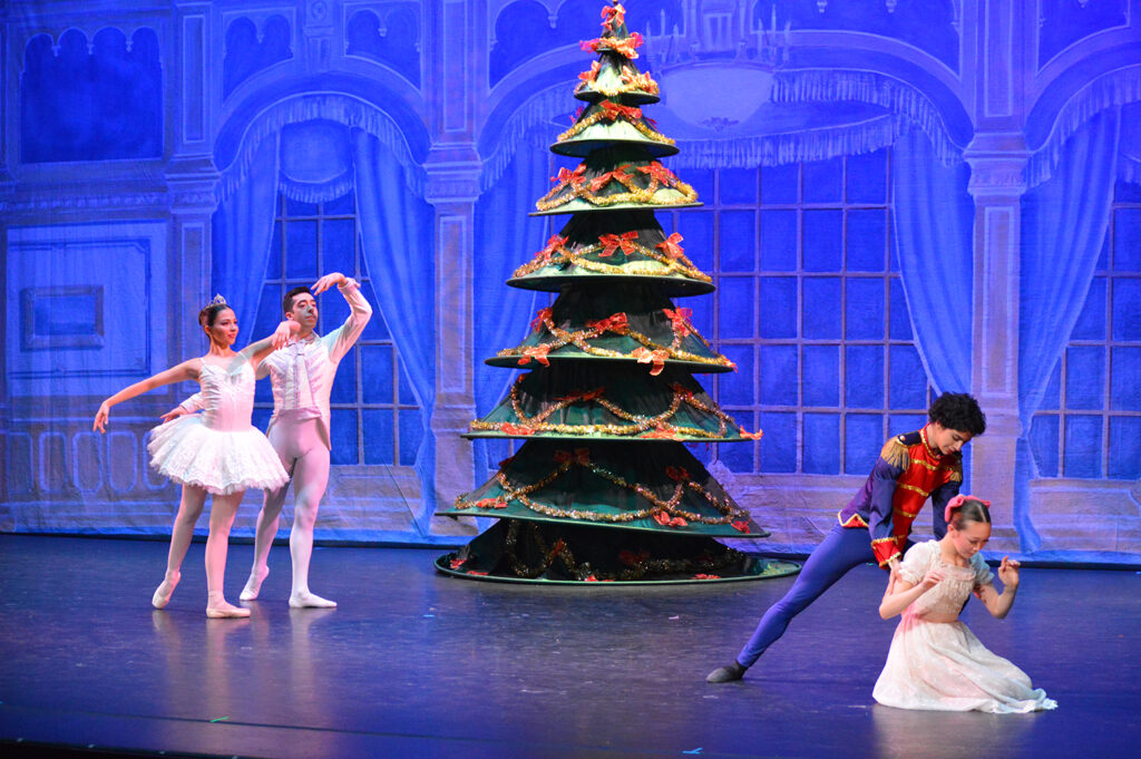 Two dancers in background and two younger dancers in foreground with a Christmas tree