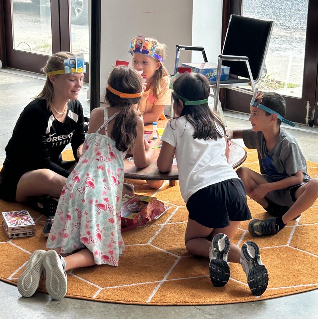 Group of kids and one adult sit on the floor with crowns on their heads