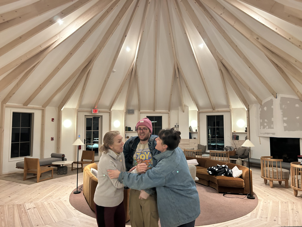 Two women stand on either side of a man, squeezing him.