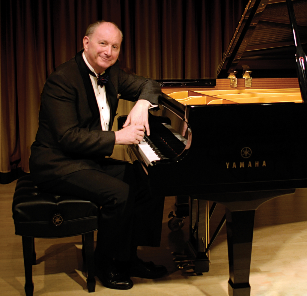 Man in a tuxedo sits at a grand piano