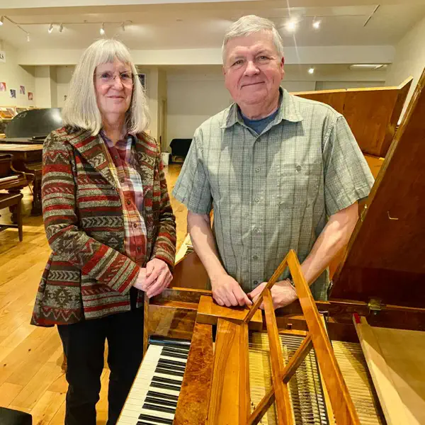 A woman and a man stand behind a historic piano.