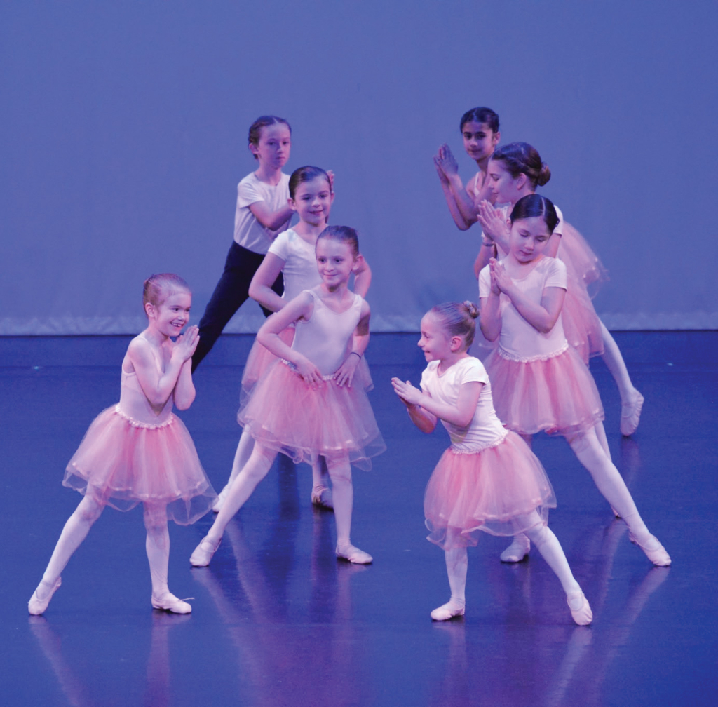 A group of young girls in pink tutus dance on stage