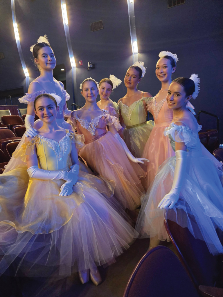 A group of girls in ballet costumes stand in a theater.