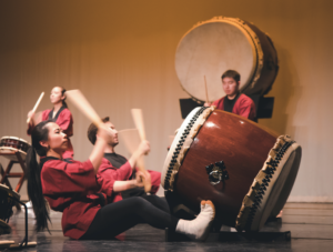 A group of people sit on a stage playing large taiko drums.