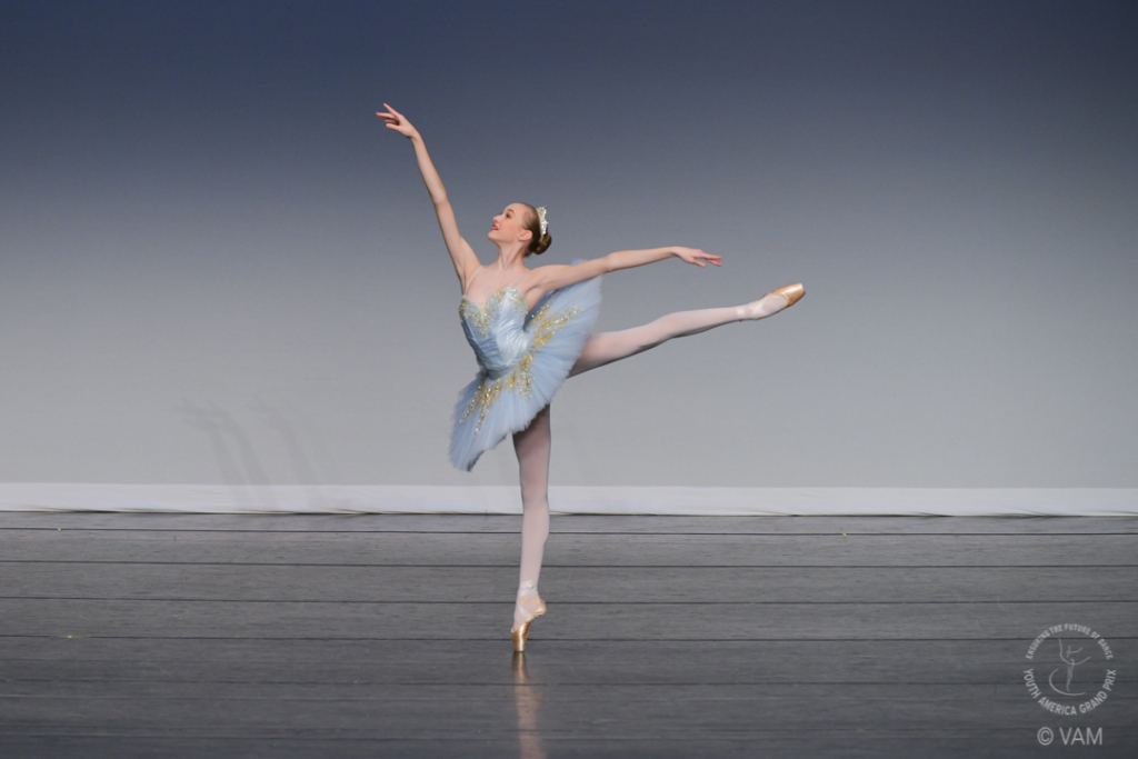 Young woman in blue tutu in arabesque pose on a stage.