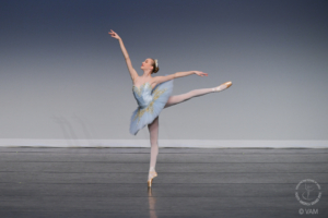Young woman in blue tutu in arabesque pose on a stage.