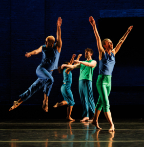 Four dancers dressed in blue and green on a stage in various poses