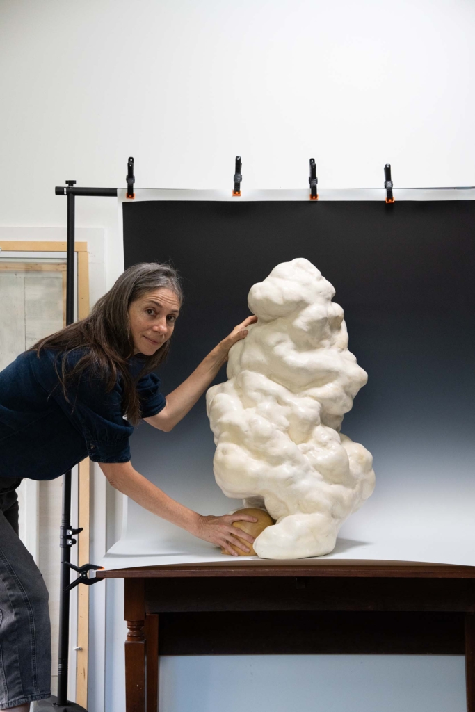 An artist dressed in black with a cloud sculpture