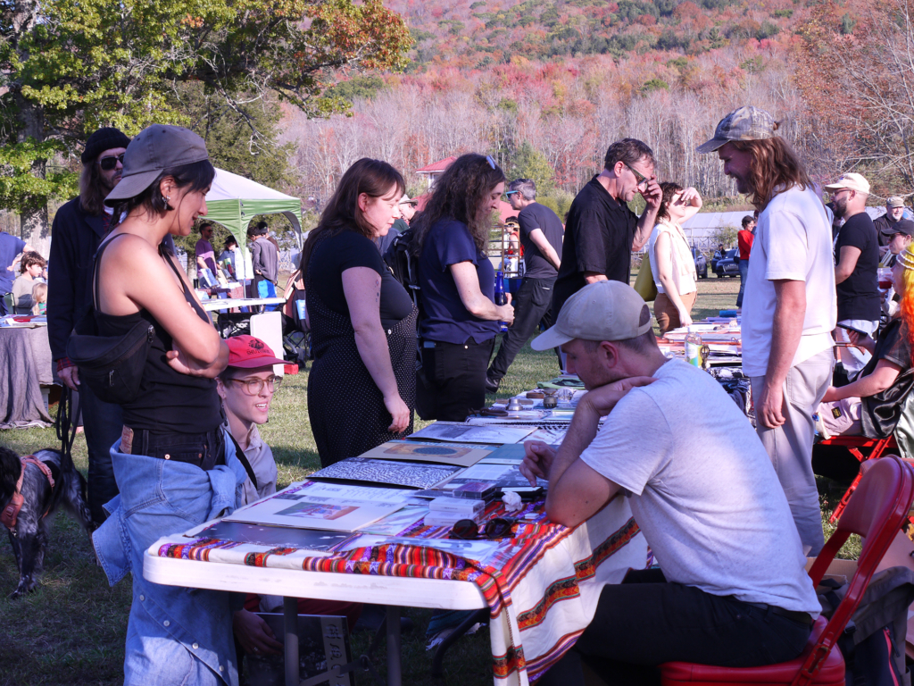 A group of people stand around a table with mountains in the background.